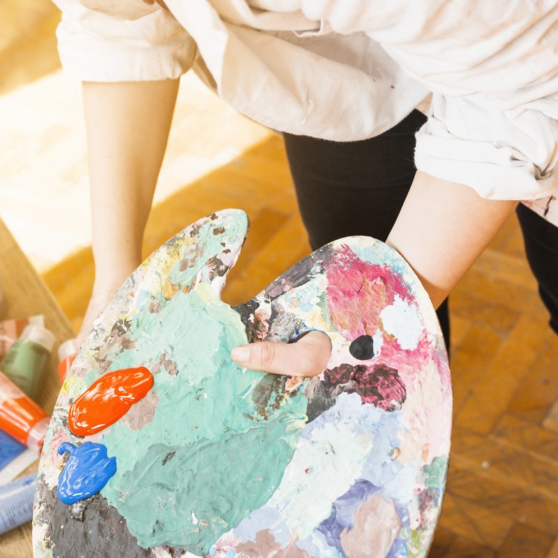 female-artist-s-hand-holding-messy-paint-palette-workshop
